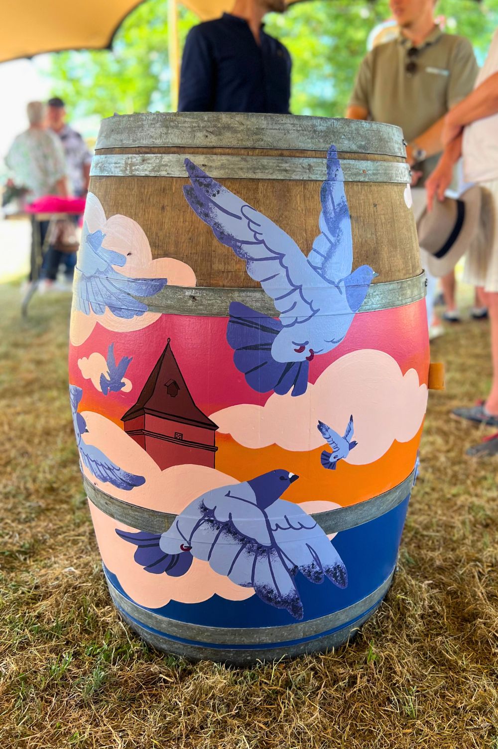 un vol de pigeons peint à la main sur une barrique en bois avec le haut d'un pigeonnier et des nuages rose clair.