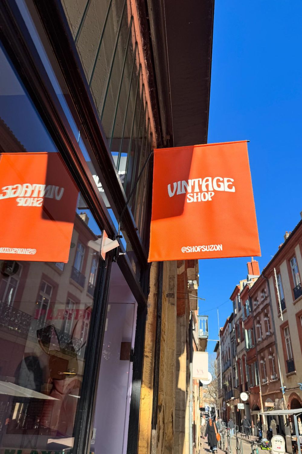 enseigne drapeau peint à la main avec l'inscription "vintage shop" et en dessous @suzonshop. Le drapeau est accroché à la devanture de la friperie Suzon à Toulouse.