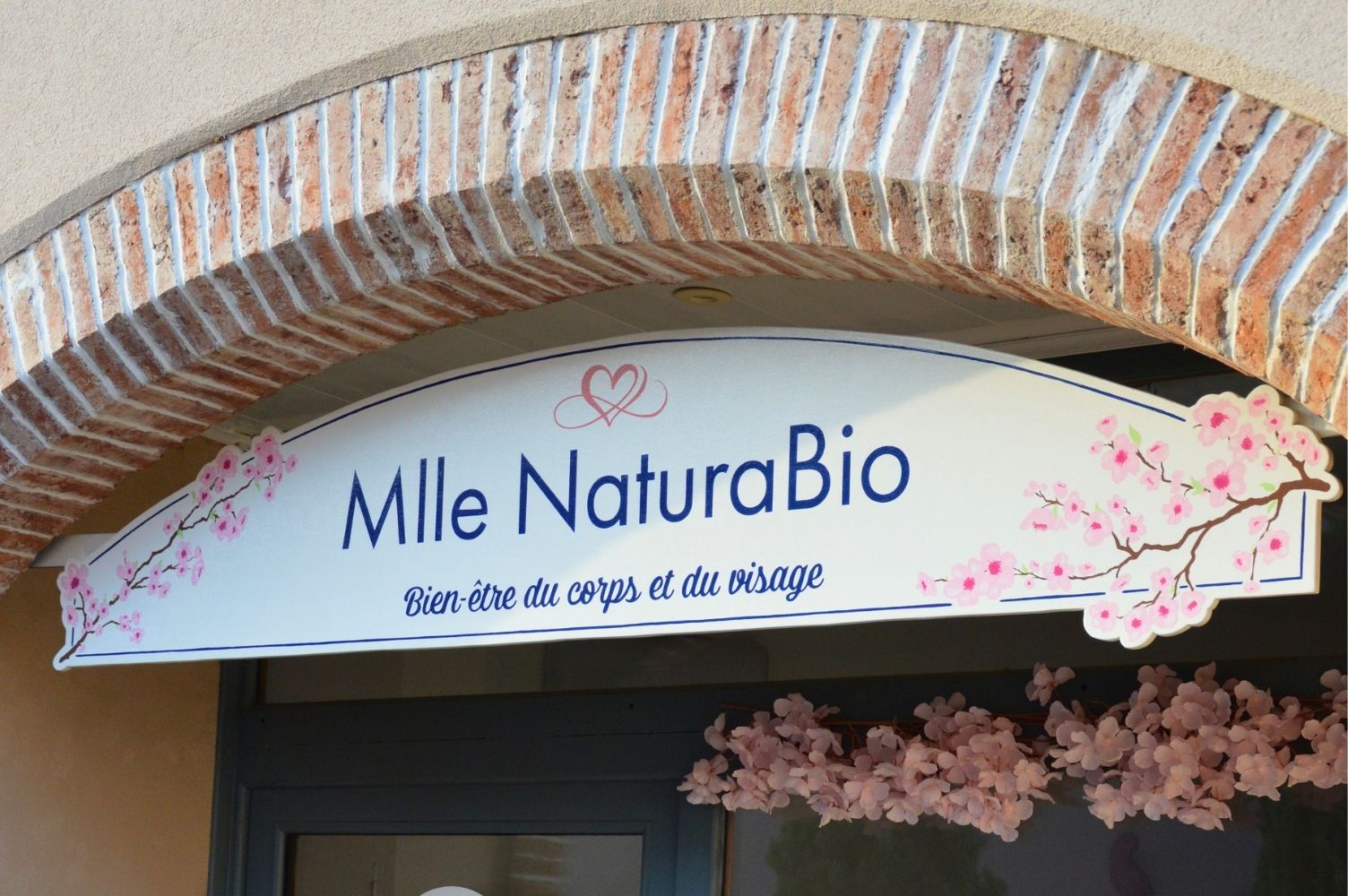 Enseigne commerciale sur la devanture d'un institut de beauté du nom de Mlle NaturaBio, avec l'inscription en bas "bien-être du corps et du visage"
