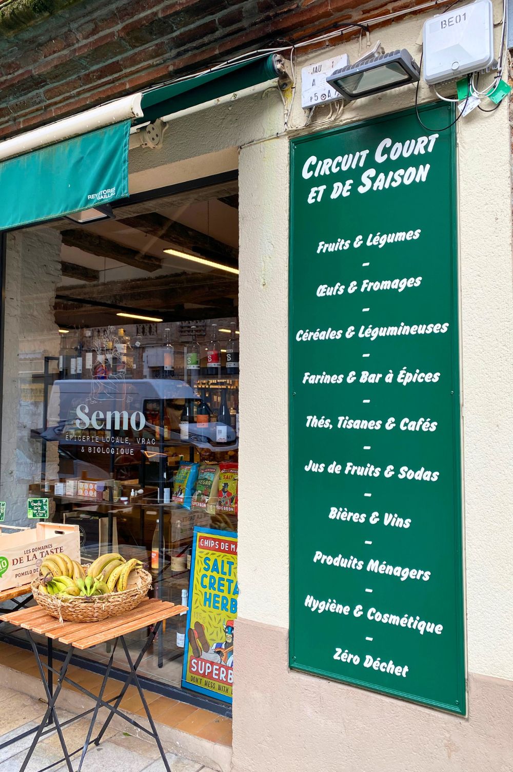 panneau enseigne en bois peint avec la liste des aliments qu'on peut trouver à l'intérieur de l'épicerie bio. Le titre indique "circuits courts et de saison" suivi de la liste des aliments et boissons.