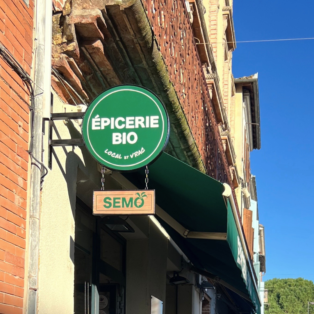 enseigne vintage moderne d'une épicerie bio (ce qui est écrit dans le cercle vert), et un encadré qui indique le nom de la boutique SEMO sur un écriteau en bois suspendu par des chaînes en métal