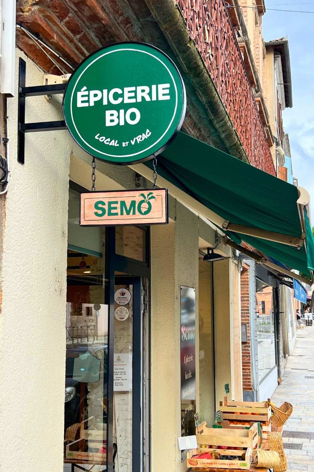 enseigne ronde en bois peint pour l'épicerie bio de Gaillac. Suspendu par des chaînes, un petit panneau indique le nom de la boutique : SEMO.