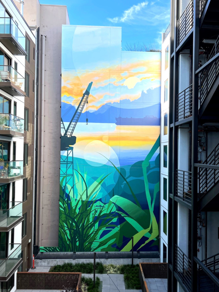 grande fresque murale sur la façade d'un immeuble à San Francisco représentant le paysage qui se trouve de l'autre côté de l'immeuble : une grue de travaux devant un coucher de soleil au second plan, et des végétaux au premier plan.