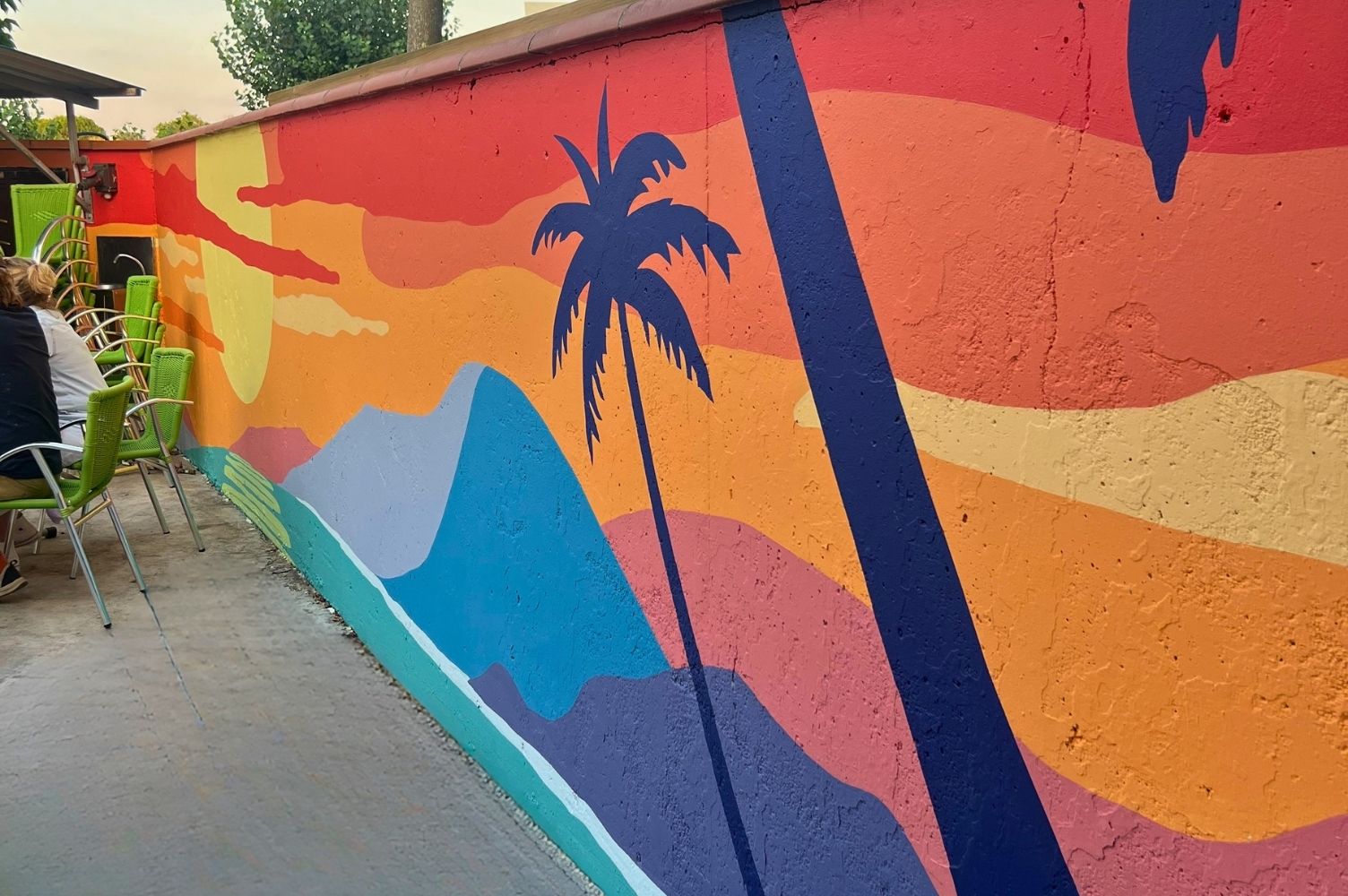 peinture sur mur représentant un palmier, une colline et un coucher de soleil.