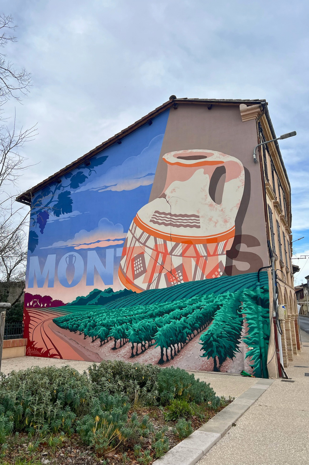 Fresque murale peinte sur une grande maison portant l'inscription MONTANS avec une amphore et des vignes.
