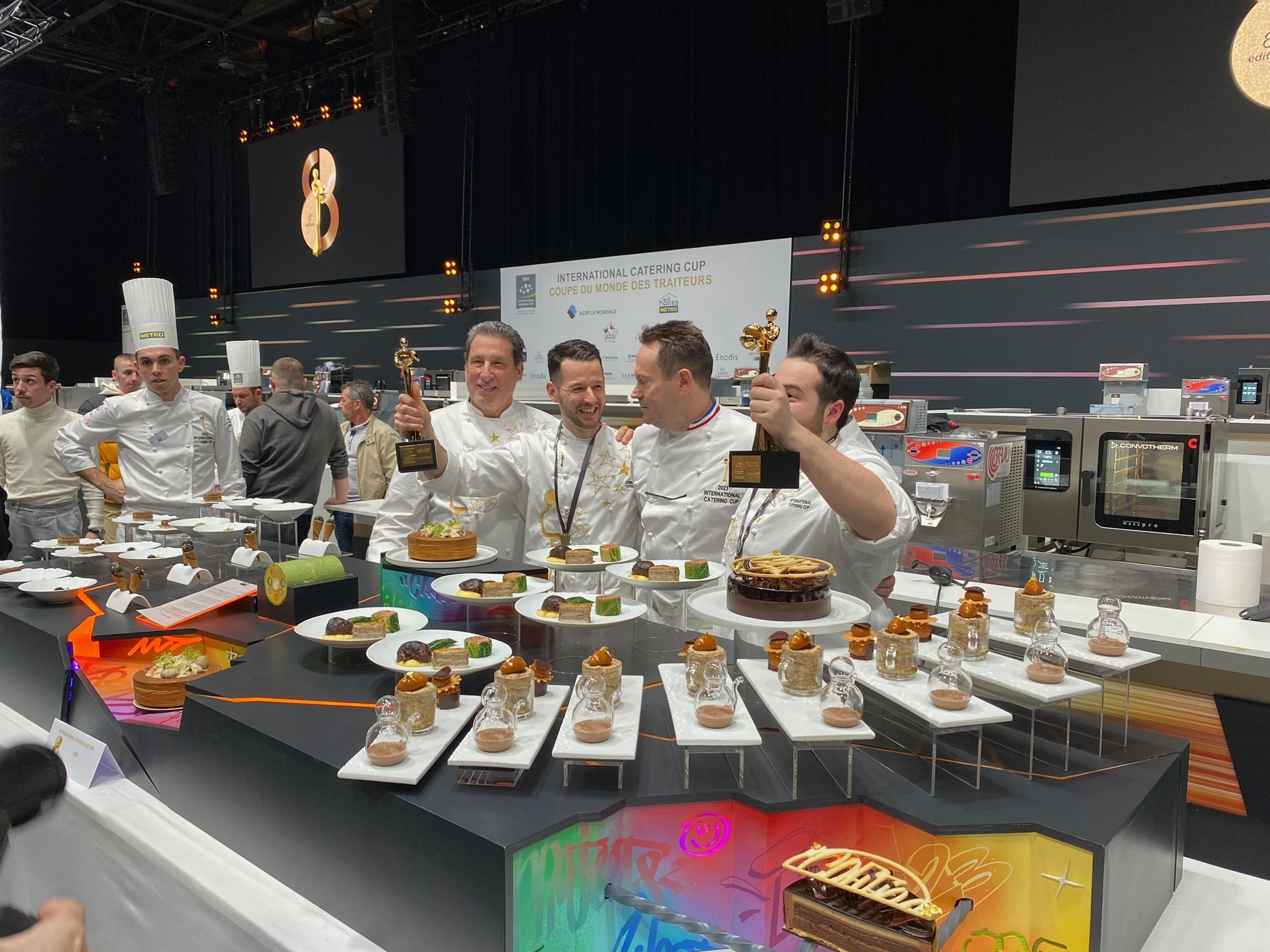 l'équipe américaine One65 qui a gagné la coupe du monde des traiteurs 2023 derrière leur table remplie de mets.