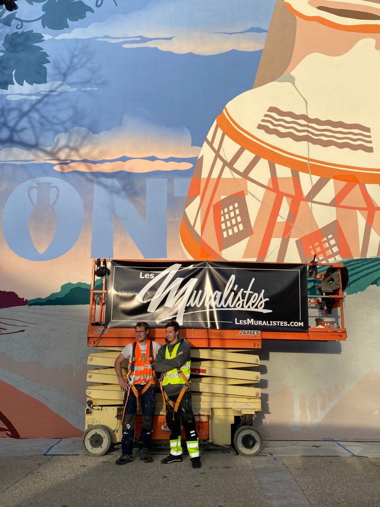 Paul en orange et Antoine en jaune, les deux frères Marnata devant la fresque qu'ils réalisent à Montans.