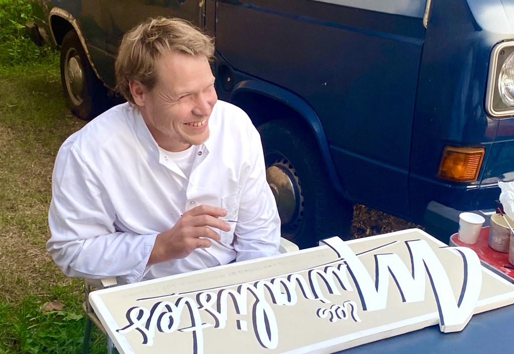 Paul Marnata peint l'enseigne de son entreprise Les Muralistes